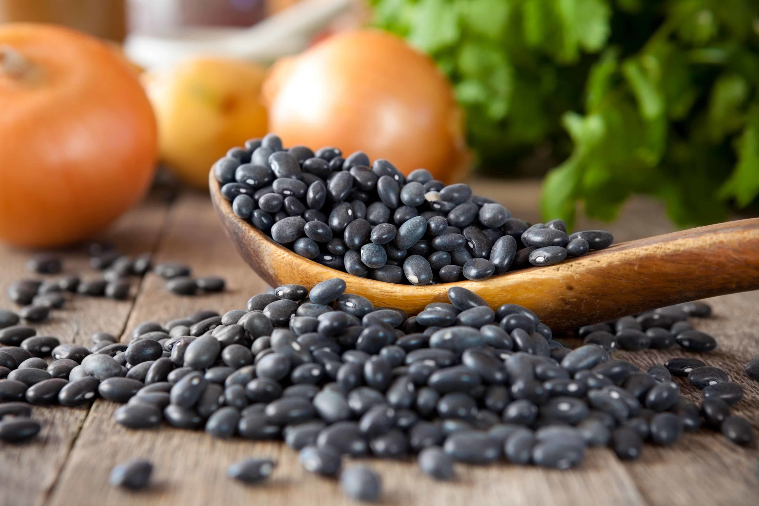 A wooden spoon with black beans and onions in the background.