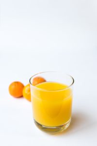 A glass of fresh orange juice with oranges in the background